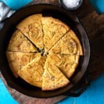 a baked farinata italian chickpea pancake sliced into pieces in a cast iron skillet next to a bowl of flaky sea salt.