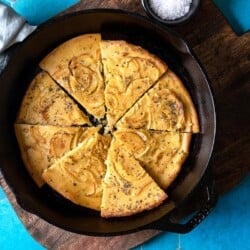 a baked farinata italian chickpea pancake sliced into pieces in a cast iron skillet next to a bowl of flaky sea salt.