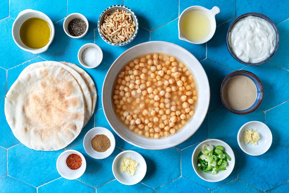 ingredients for Fatteh including olive oil, spices, pine nuts, garlic, lemon juice, tahini, Greek yogurt, green onions, chickpeas and pita bread.