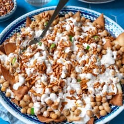Fatteh (Spiced Chickpeas with Crispy Pita and Garlicky Yogurt) in a bowl with a spoon next to a glass of water.