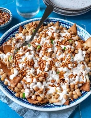 Fatteh (Spiced Chickpeas with Crispy Pita and Garlicky Yogurt) in a bowl with a spoon next to a glass of water.