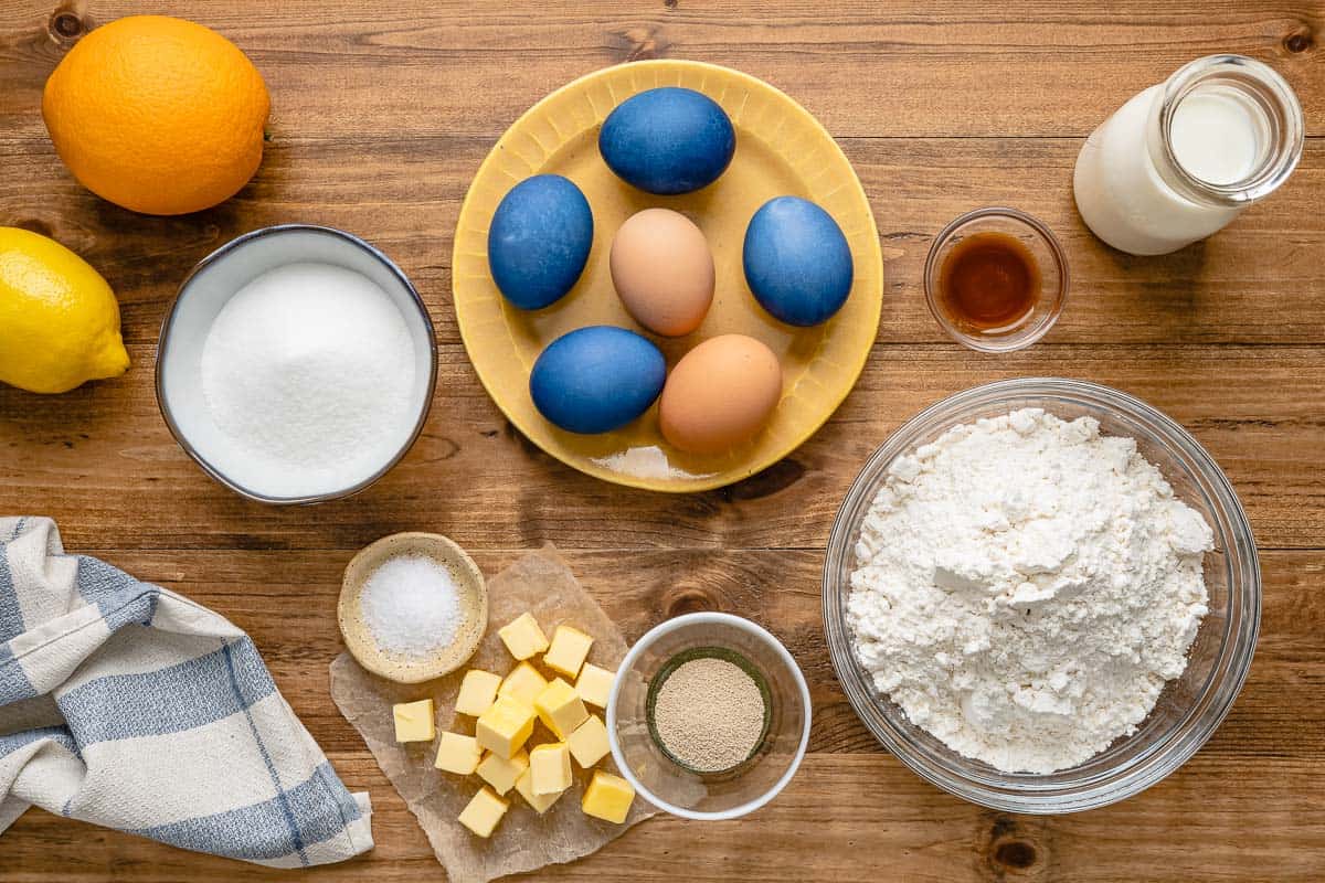 ingredients for italian easter bread including milk, yeast, sugar, eggs, flour, butter, vanilla, orange zest, lemon zest, dyed uncooked eggs, nonpareils.