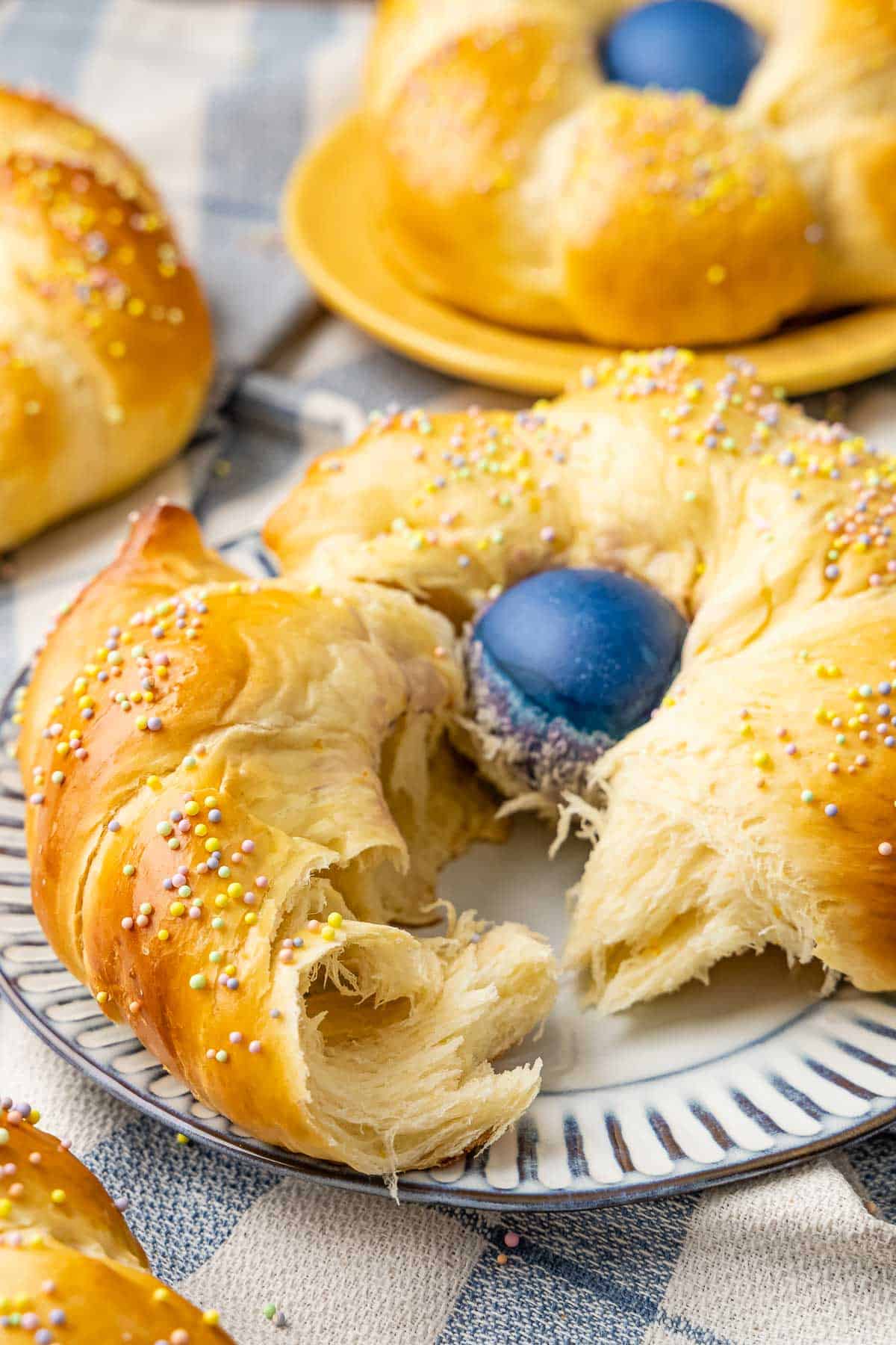 a torn piece of italian easter bread with a dyed blue egg on a plate.