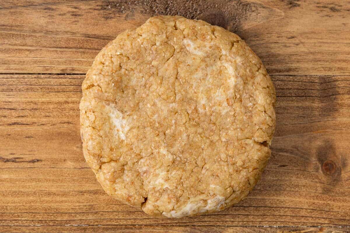 Quiche crust dough that's been flattened into a circle on a wooden counter.