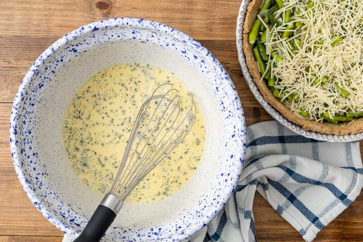 Eggs, milk, Dijon mustard, herbs and seasonings being whisked in a large bowl.