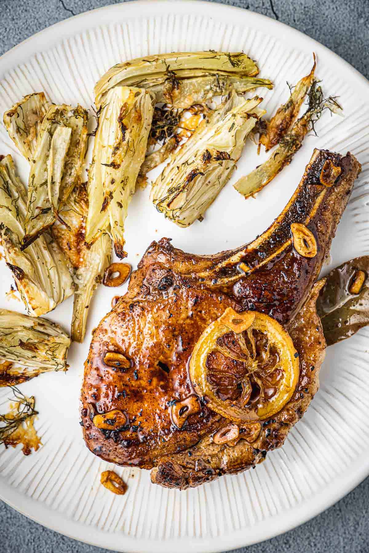 a pan seared pork chop on a plate with roasted fennel.