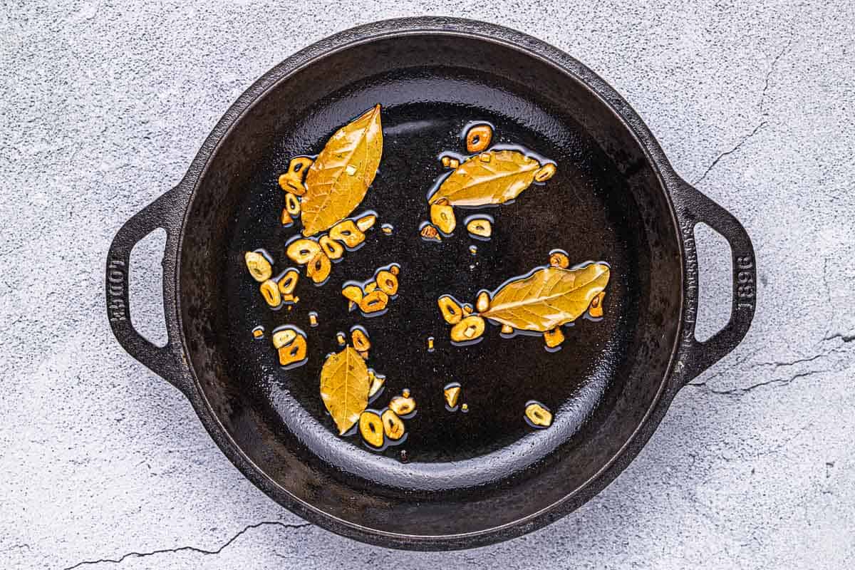 tranches d'ail et feuilles de laurier cuisant dans une poêle en fonte.
