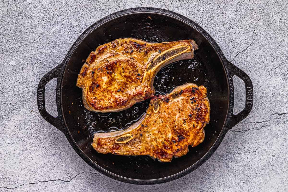 two pan seared pork chops in a cast iron skillet.