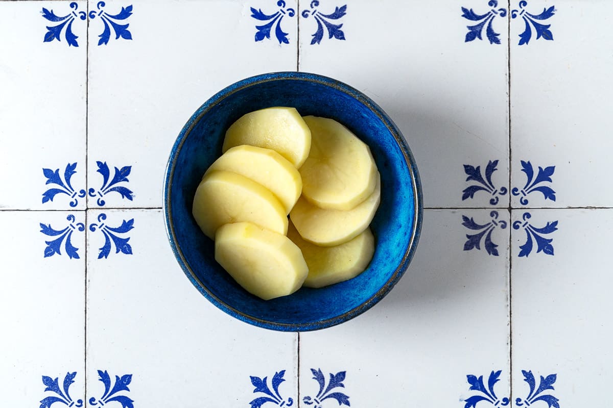 Uncooked sliced potatoes in a blue bowl.