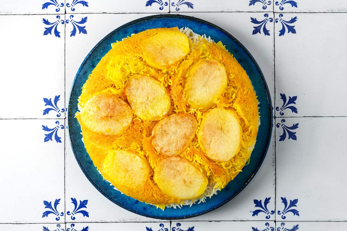 Overhead shot of golden Persian Rice with Potato Tahdig on a blue plate.