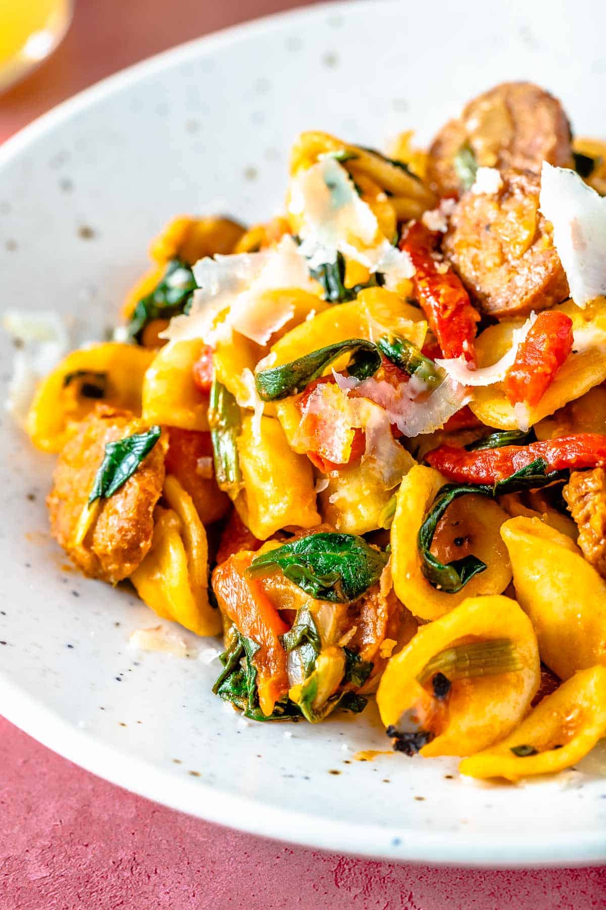 Closeup of orecchiette pasta with spicy Spanish chorizo, shaved cheese, and wilted spinach.