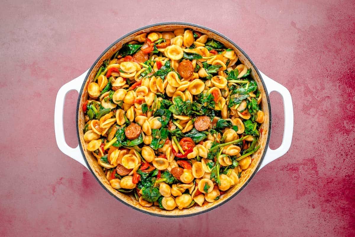 Chorizo pasta in a Dutch oven with wilted spinach.
