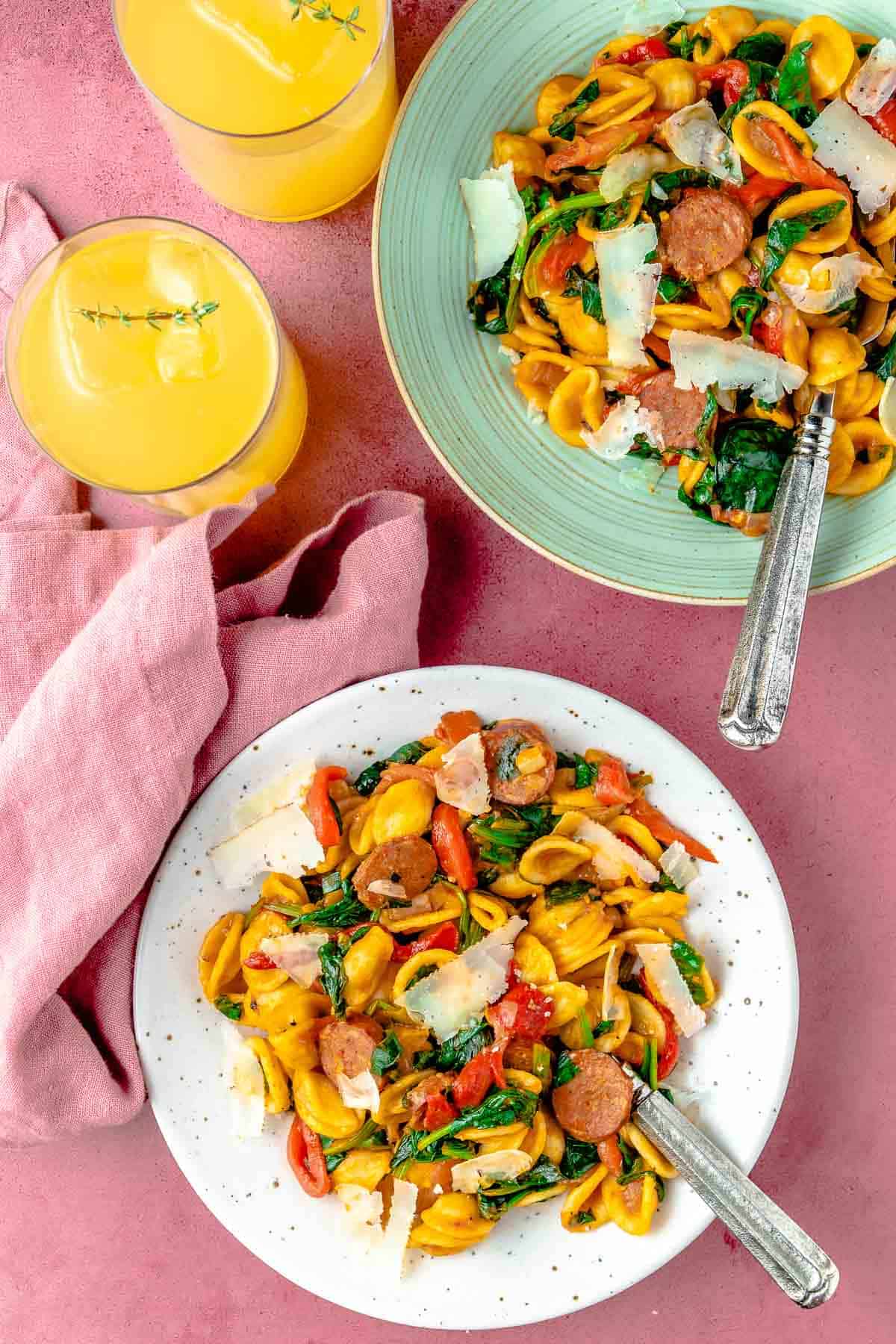 Two bowls of chorizo pasta with wilted spinach, shaved manchego cheese, and a couple of cocktails on the side.