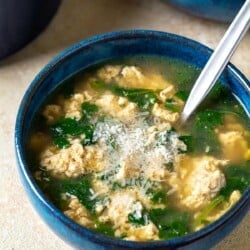 Close up of a blue bowl with Stracciatella Soup and freshly grated Parmesan cheese.