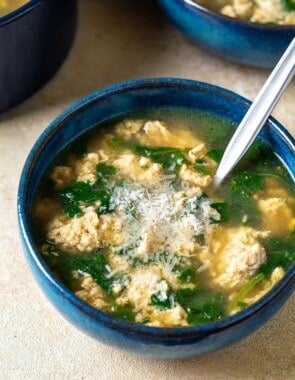 Close up of a blue bowl with Stracciatella Soup and freshly grated Parmesan cheese.