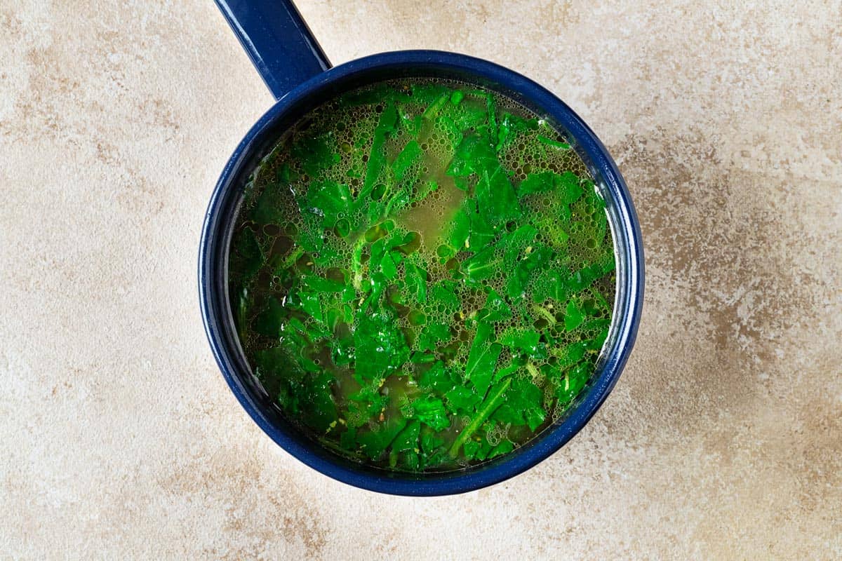 Blue pot of chicken broth with wilted spinach inside.