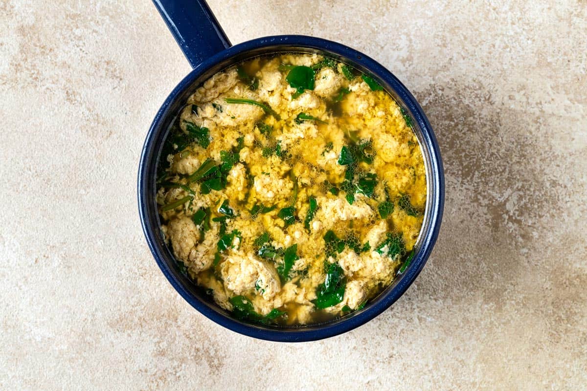 Overhead shot showing a pot of Stracciatella Soup with cooked eggs and wilted spinach.