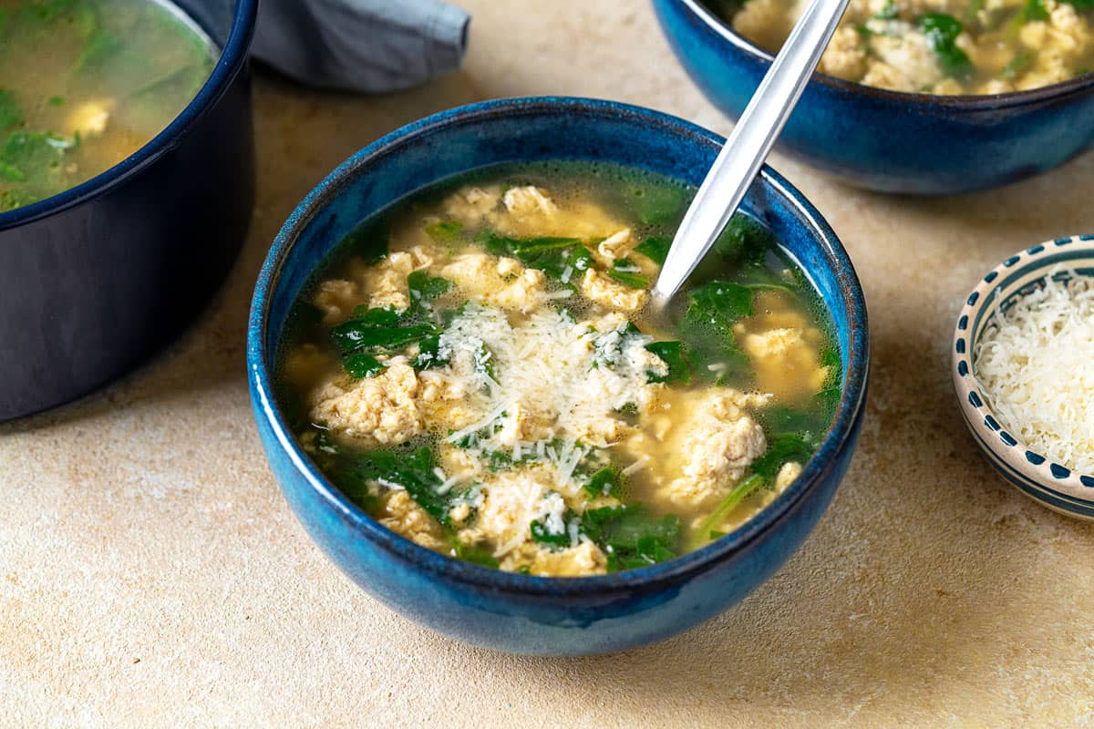 Closeup of a bowl of Stracciatella Soup with a spoon inside.