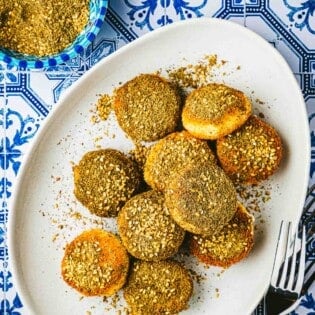 10 fried goat cheese slices on plate next to a bowl of za'ata and a fork.