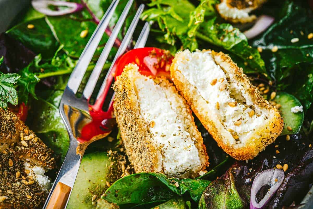 a fried goat cheese slice cut in half on a bed of salad with a fork.