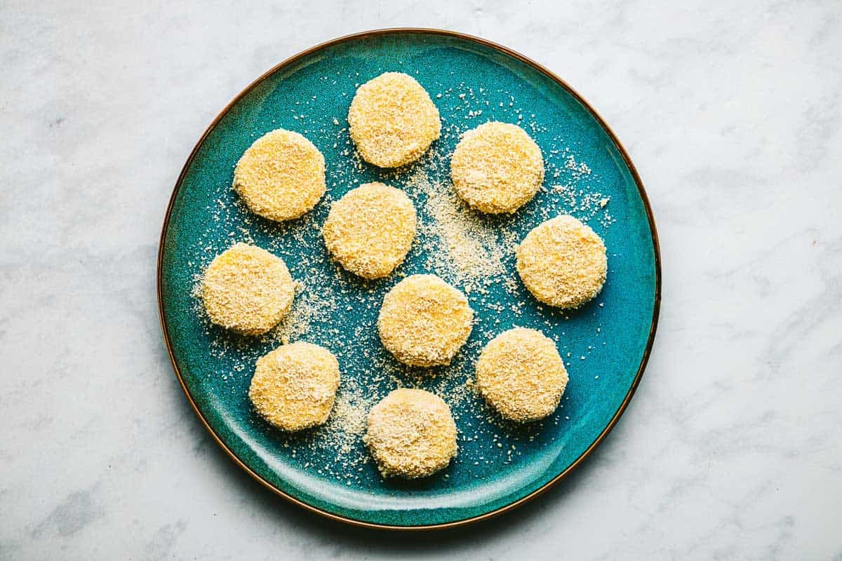 10 goat cheese slices coated in breadcrumbs on plate.