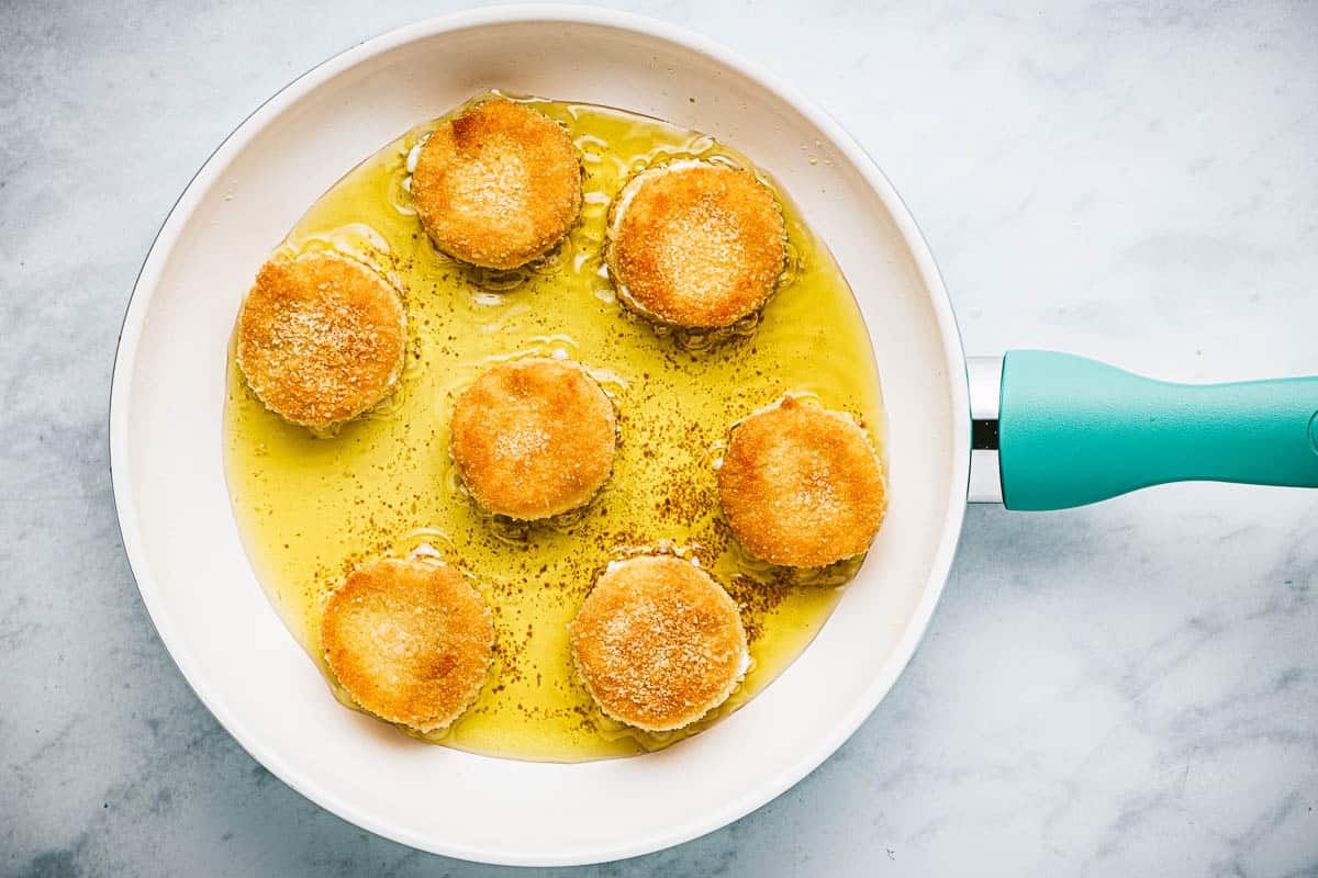 7 goat cheese slices frying in olive oil in a skillet.