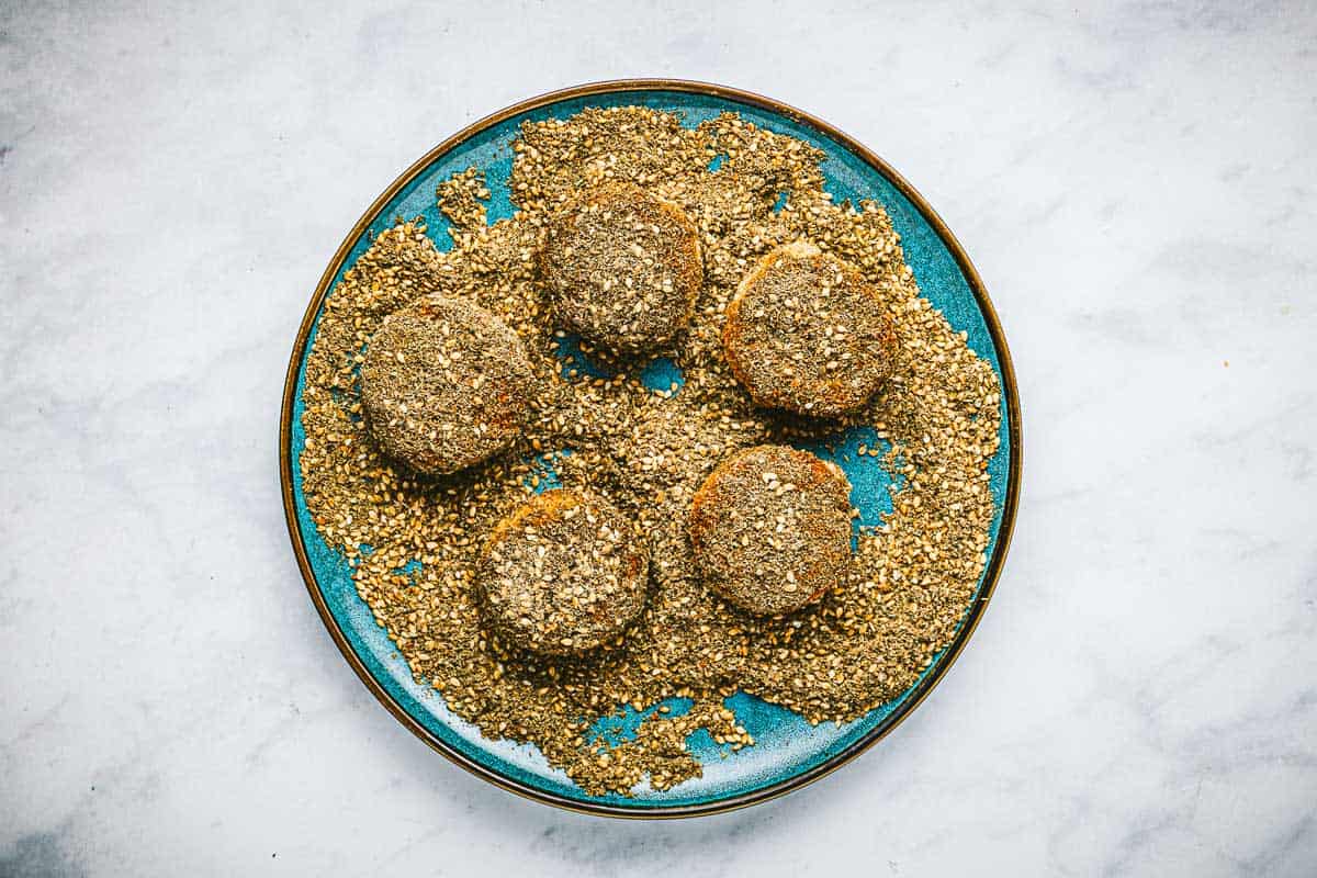 five fried goat cheese slices being coated in za'atar on a plate.