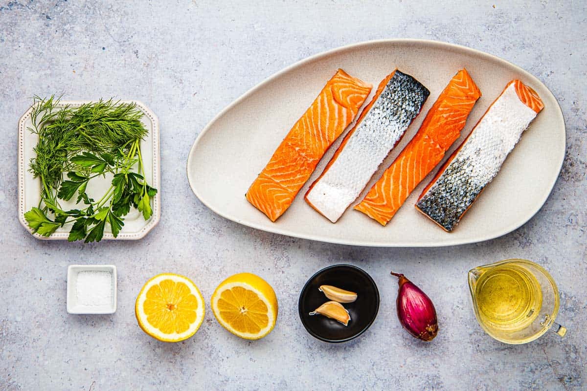 ingredients for poached salmon including 4 salmon fillets lemon, garlic, shallot, white wine, parsley, dill, and kosher salt.