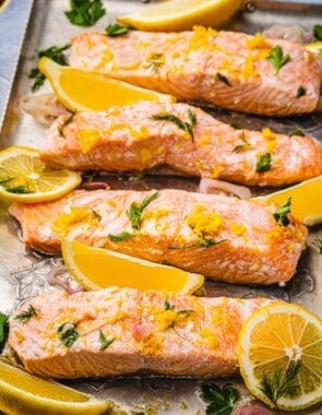 4 poached salmon fillet slices with dill, lemon, parsley and shallots on a serving tray.