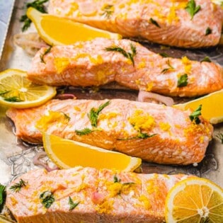 4 poached salmon fillet slices with dill, lemon, parsley and shallots on a serving tray.