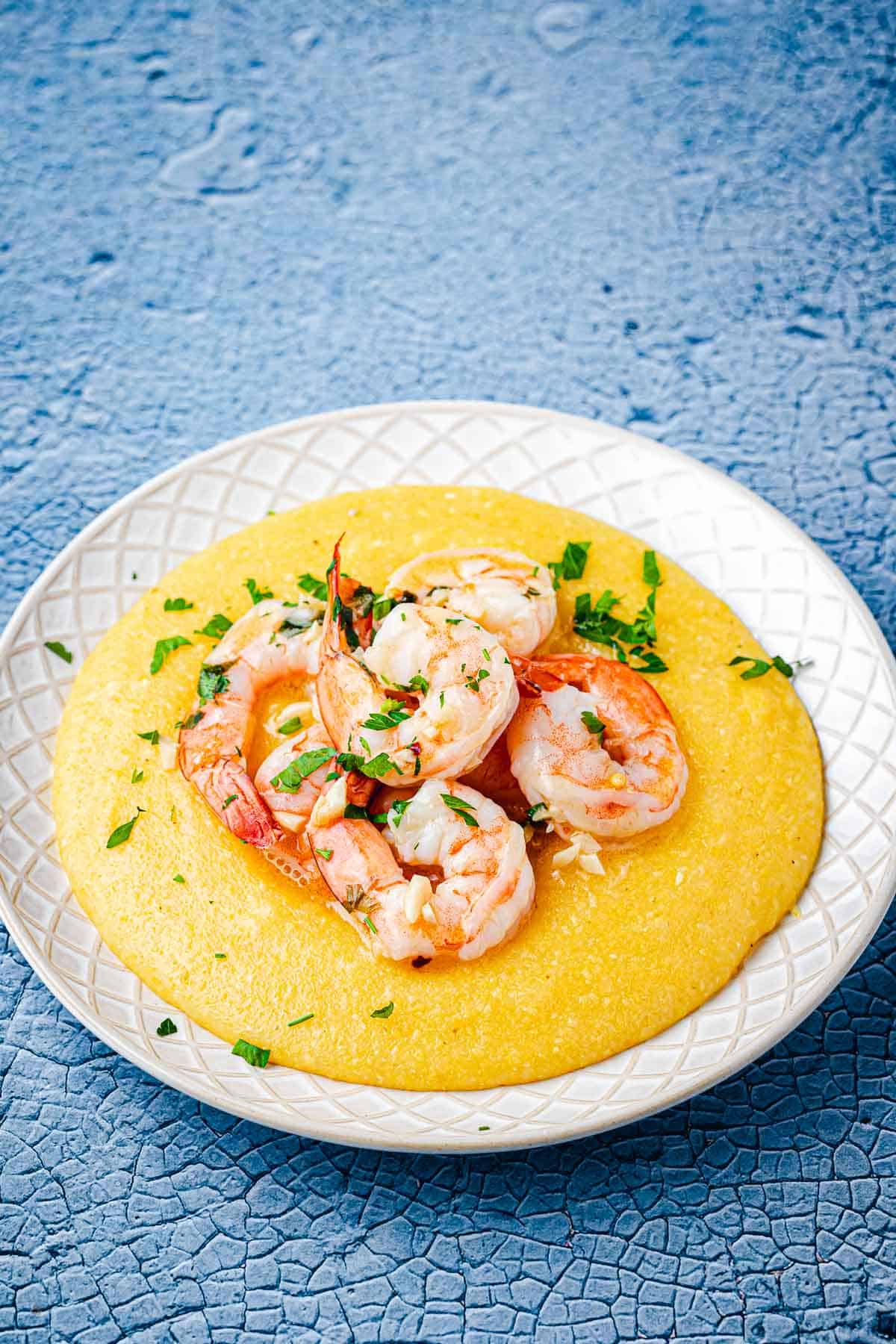 a plate of polenta and shrimp garnished with parsley.