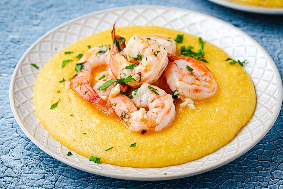 a plate of polenta and shrimp garnished with parsley.