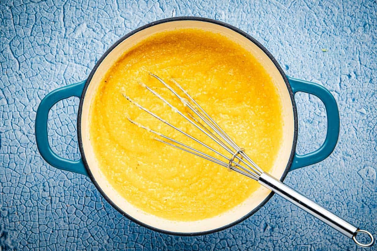 polenta in a pot being stirred with a whisk.