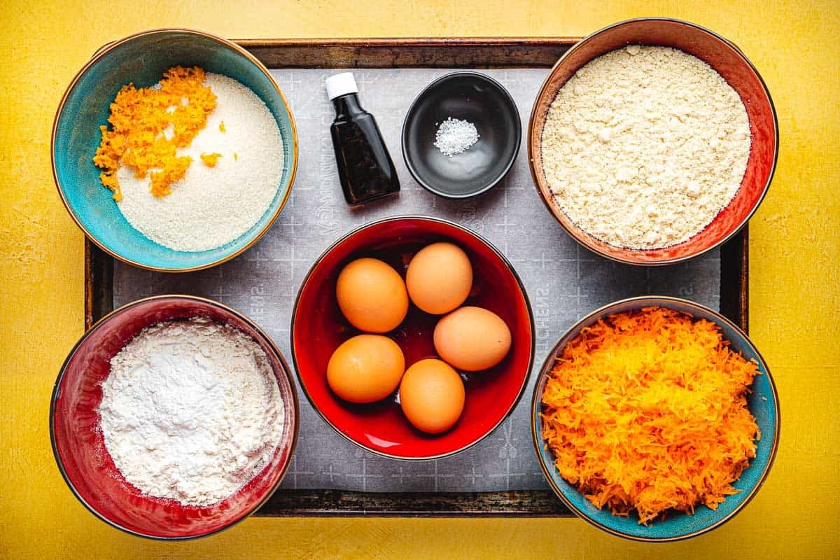 ingredients for Torta di Carote (Italian Carrot Cake) including almond flour, all purpose flour, baking powder, sugar, orange zest, eggs, shredded carrot, almond extract, and kosher salt.