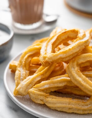Stack of churros on a gray plate with Spanish drinking chocolate in the background.