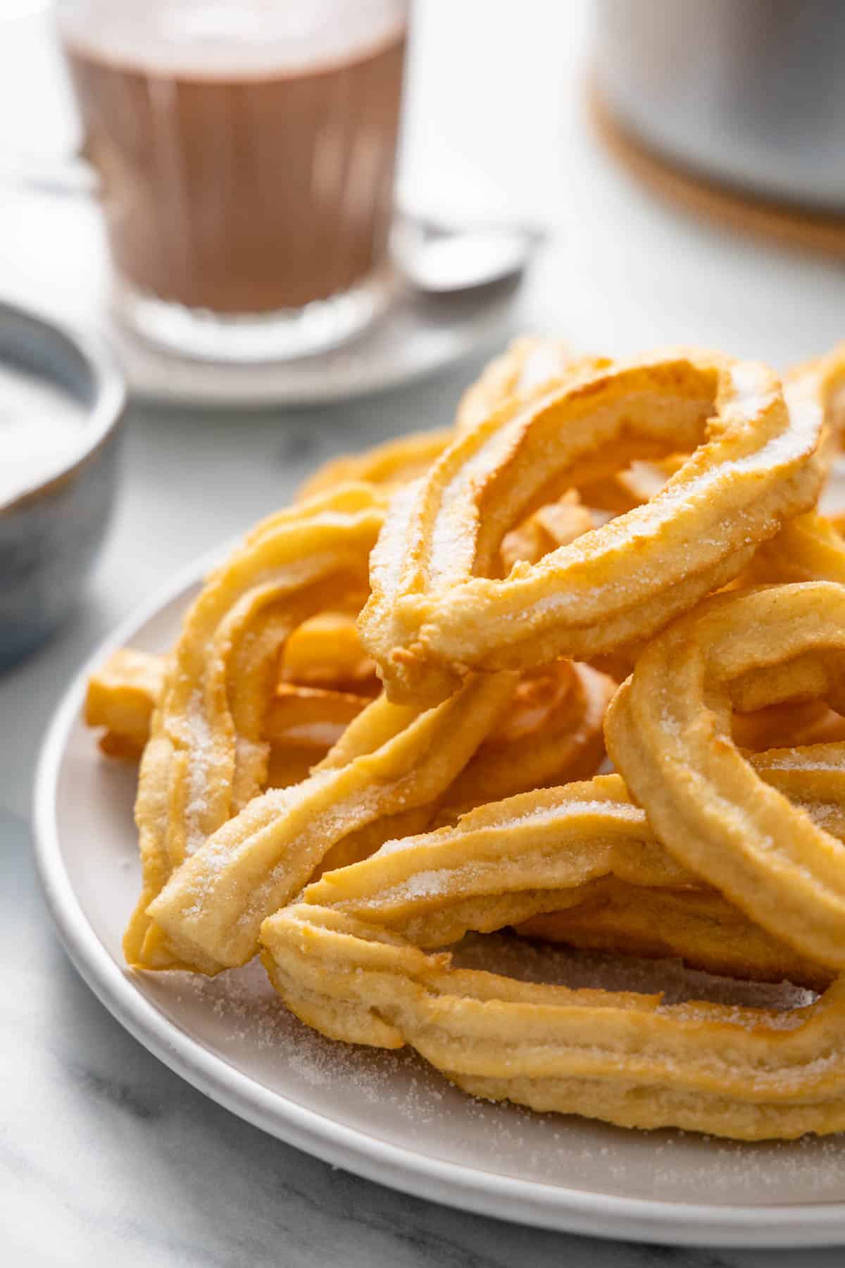 Stack of churros on a gray plate with Spanish drinking chocolate in the background.