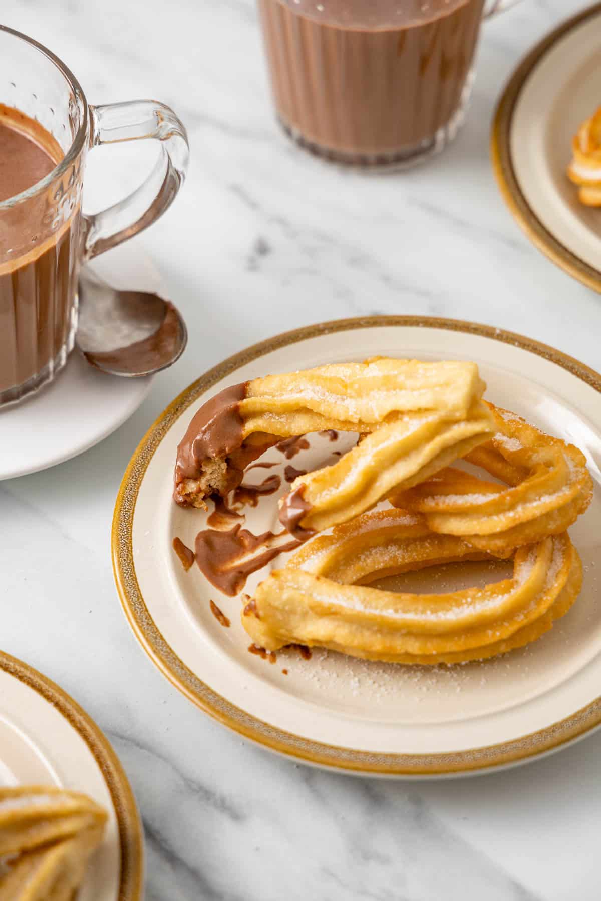 Chocolate dunked churros on a gold-rimmed plate with a bite taken out.