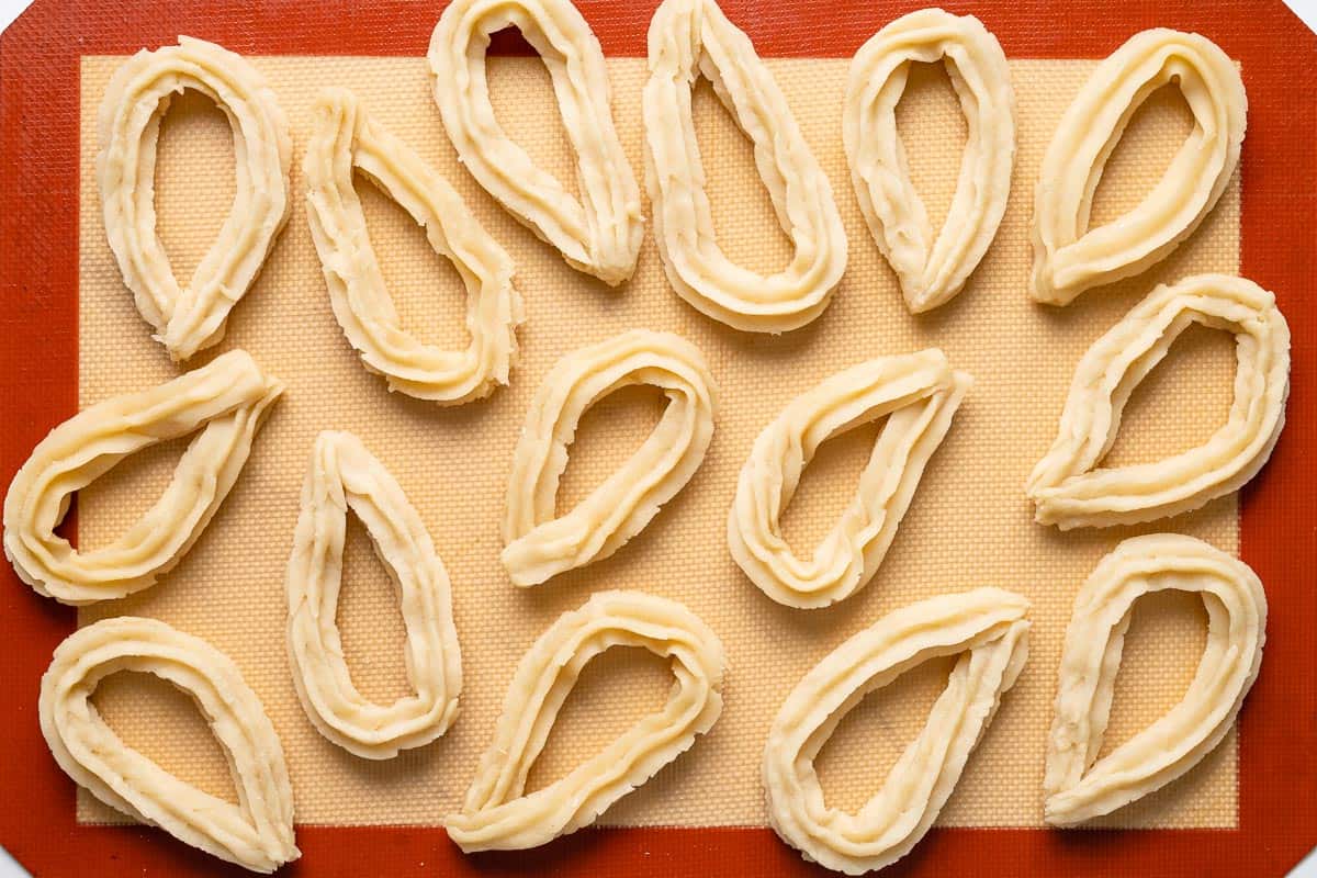 Uncooked shaped churros on a silicone baking mat.