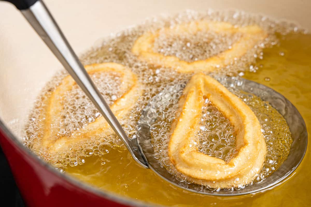 Three churros frying in bubbling oil.