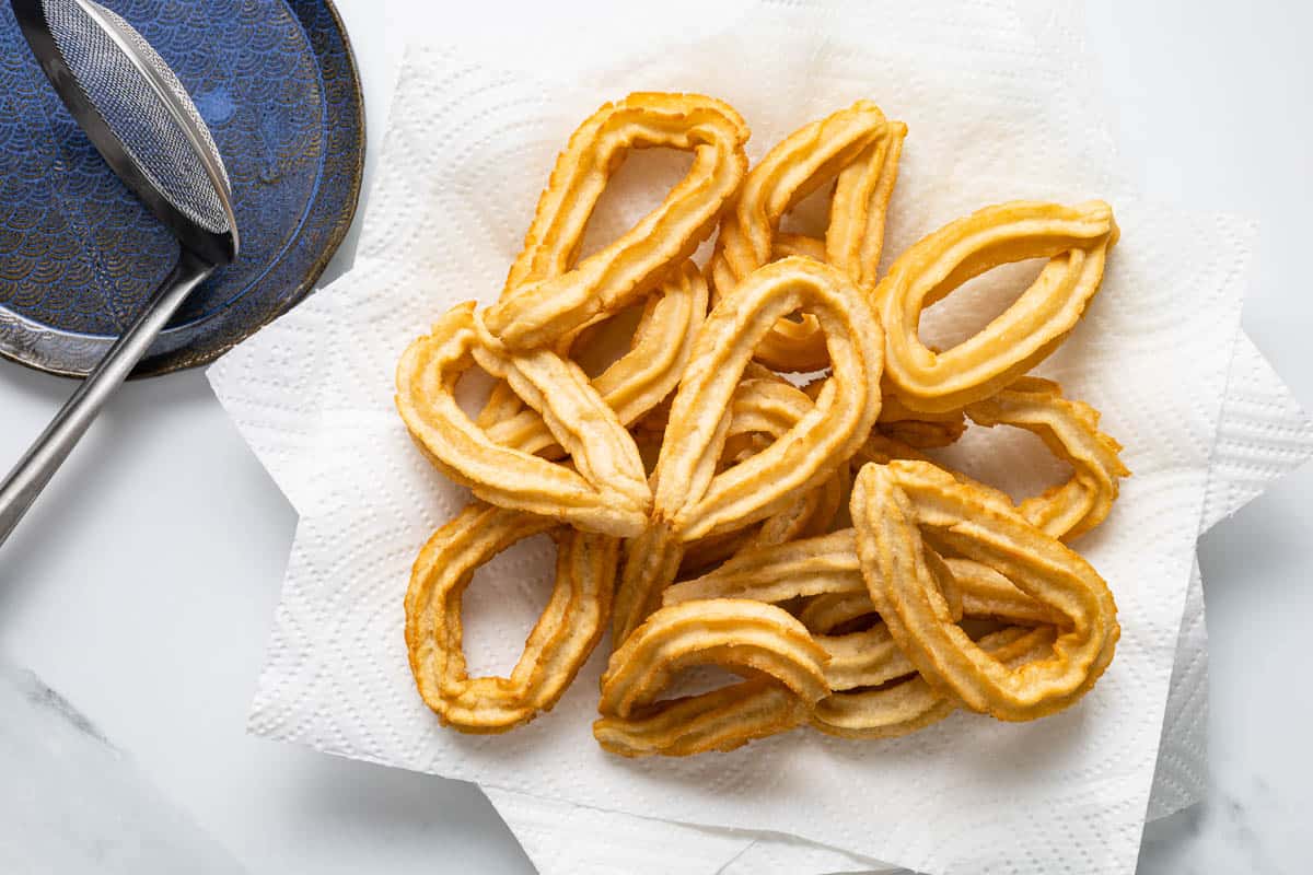 Stack of freshly fried churros draining on paper towels.