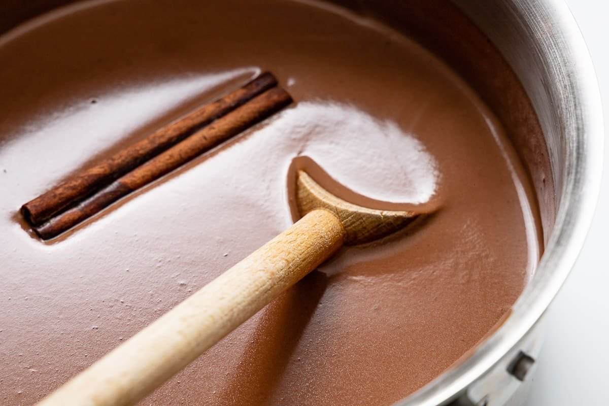 Spanish drinking chocolate in a pot with a wooden spoon and cinnamon stick.