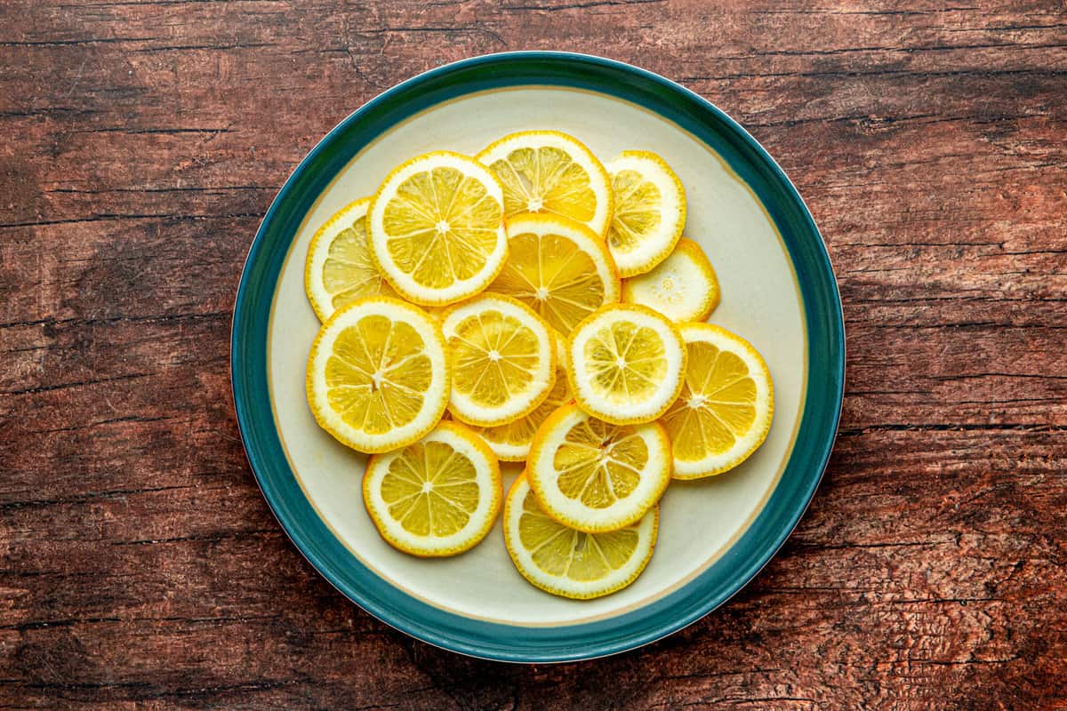 Raw slices of lemon on a green-rimmed plate with a wooden background.