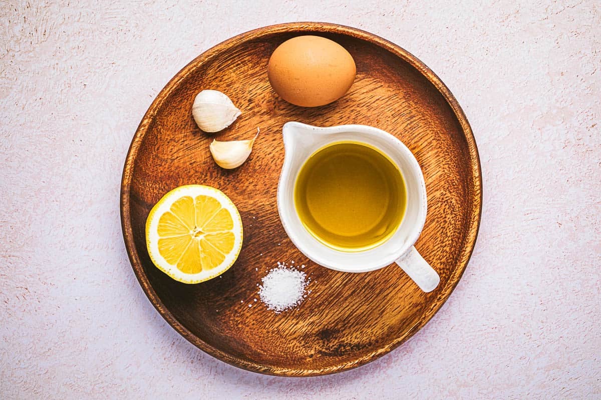 ingredients for garlic aioli including garlic, an egg, lemon, salt and olive oil.