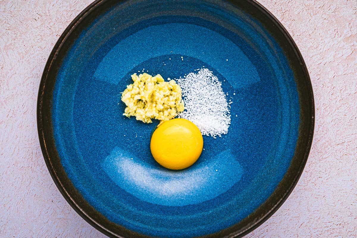 an egg yolk, minced garlic and salt in a bowl.