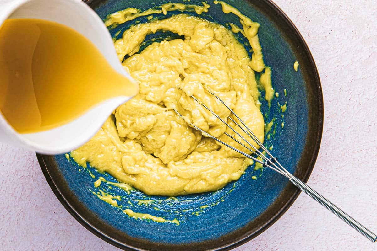 olive oil being slowly added to the garlic aioli in a bowl with a whisk.