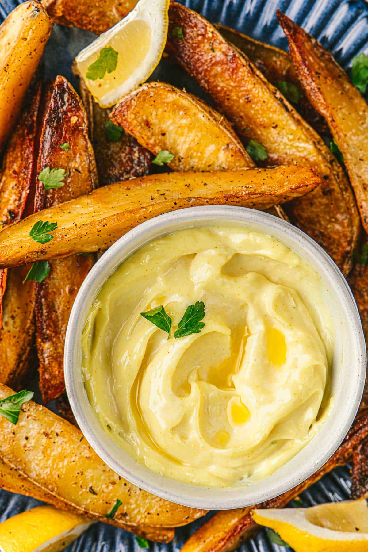 a bowl of garlic aioli on a plate with potato wedges and lemons.