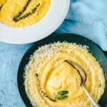 two bowls of polenta topped with parmigiano reggiano cheese and a sprig of thyme.