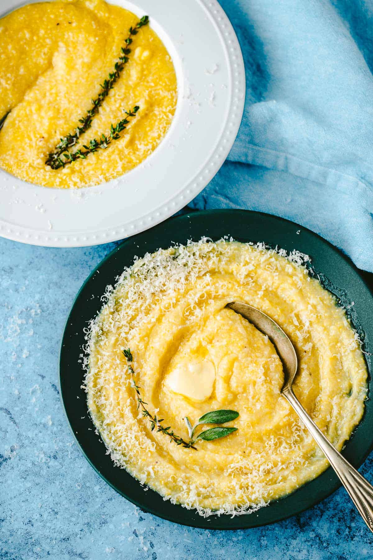 two bowls of polenta topped with parmigiano reggiano cheese and a sprig of thyme.