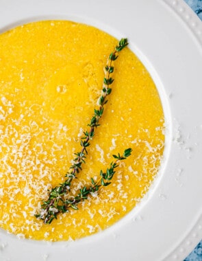 close up of a bowl of polenta topped with parmigiano reggiano cheese and a sprig of thyme.