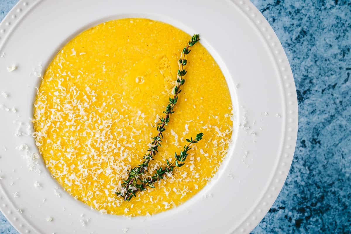 close up of a bowl of polenta topped with parmigiano reggiano cheese and a sprig of thyme.